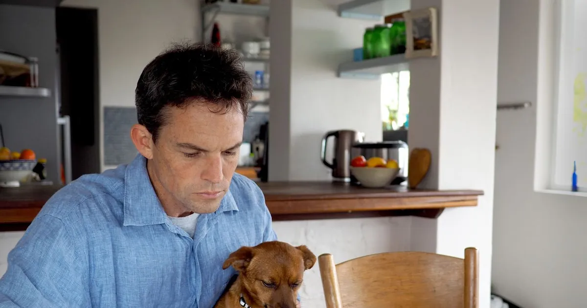 Renter reading ESA letter paperwork at a kitchen table with a small brown dog on his lap